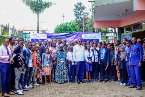 This image shows a large group of people, including both men and women, gathered outside a building at the EAUR Nyagatare campus. In the center, a few individuals are standing with a visually impaired person using a white cane, symbolizing the focus on disability inclusion. The group consists of students, faculty, and community members, standing in front of a banner for the ANSWER Project, which promotes understanding of disability and inclusion in higher education institutions. 