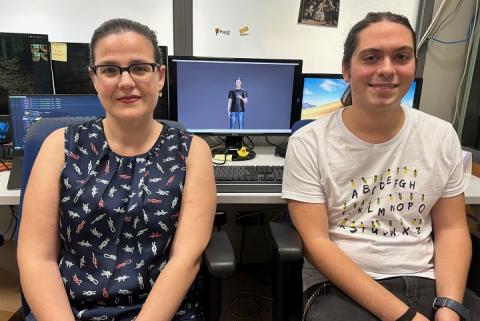 Two researchers are seated in front of monitors displaying a virtual avatar using sign language. The workspace reflects their development of a real-time sign language translation app.